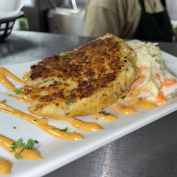 Golden-brown crab cake with coleslaw and a drizzle of orange sauce on a white rectangular plate.