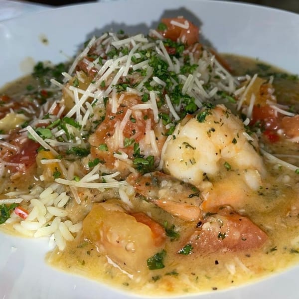 Shrimp and rice dish in a creamy sauce with diced tomatoes, topped with shredded cheese and parsley.
