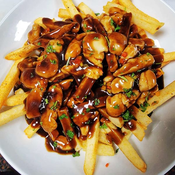 Golden french fries topped with rich brown gravy, mushrooms, and chopped parsley in a white bowl.